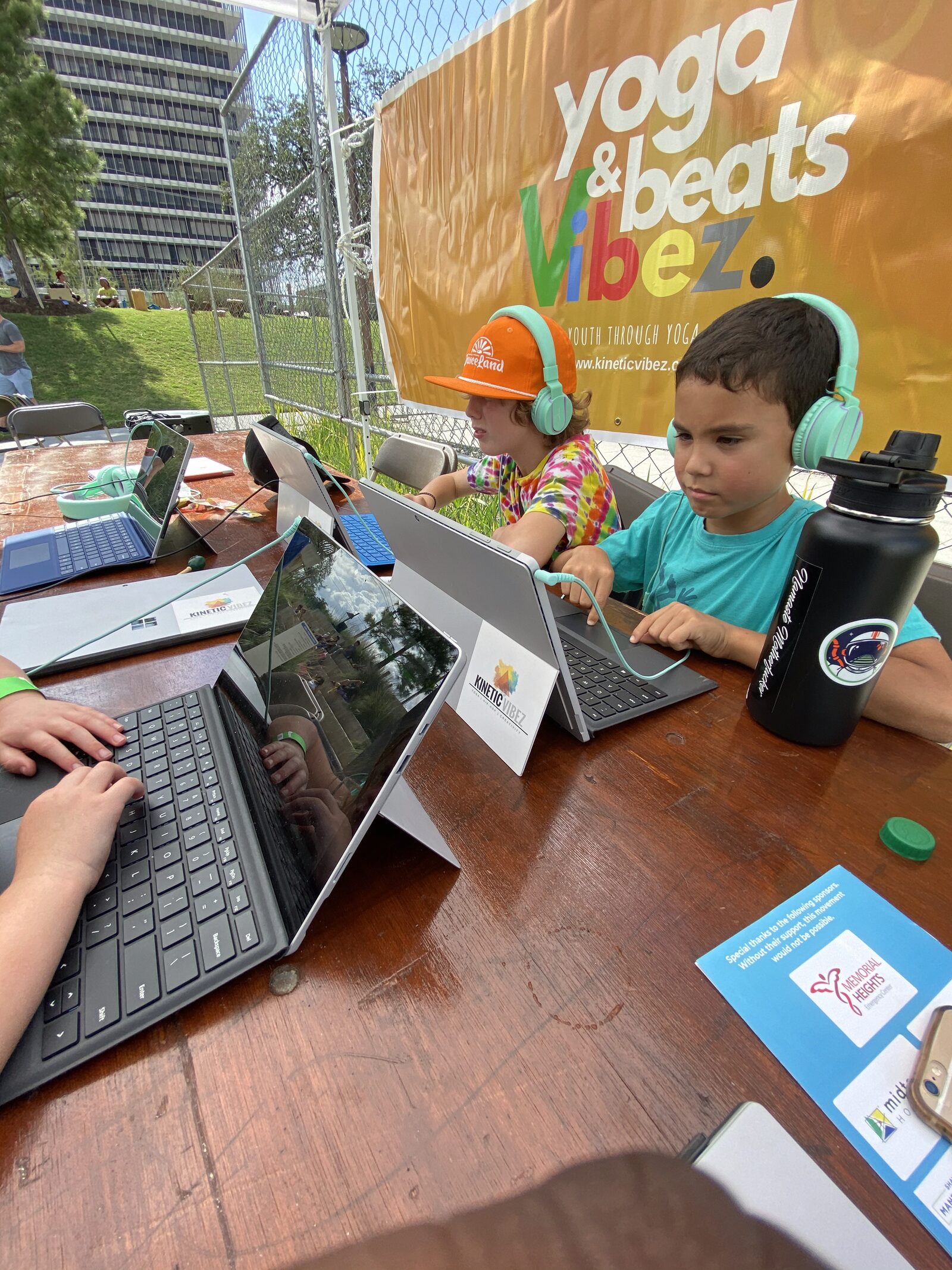 Students working on Surface tablets under the Yoga & Beats Vibez banner at a Kinetic Vibez outdoor community event