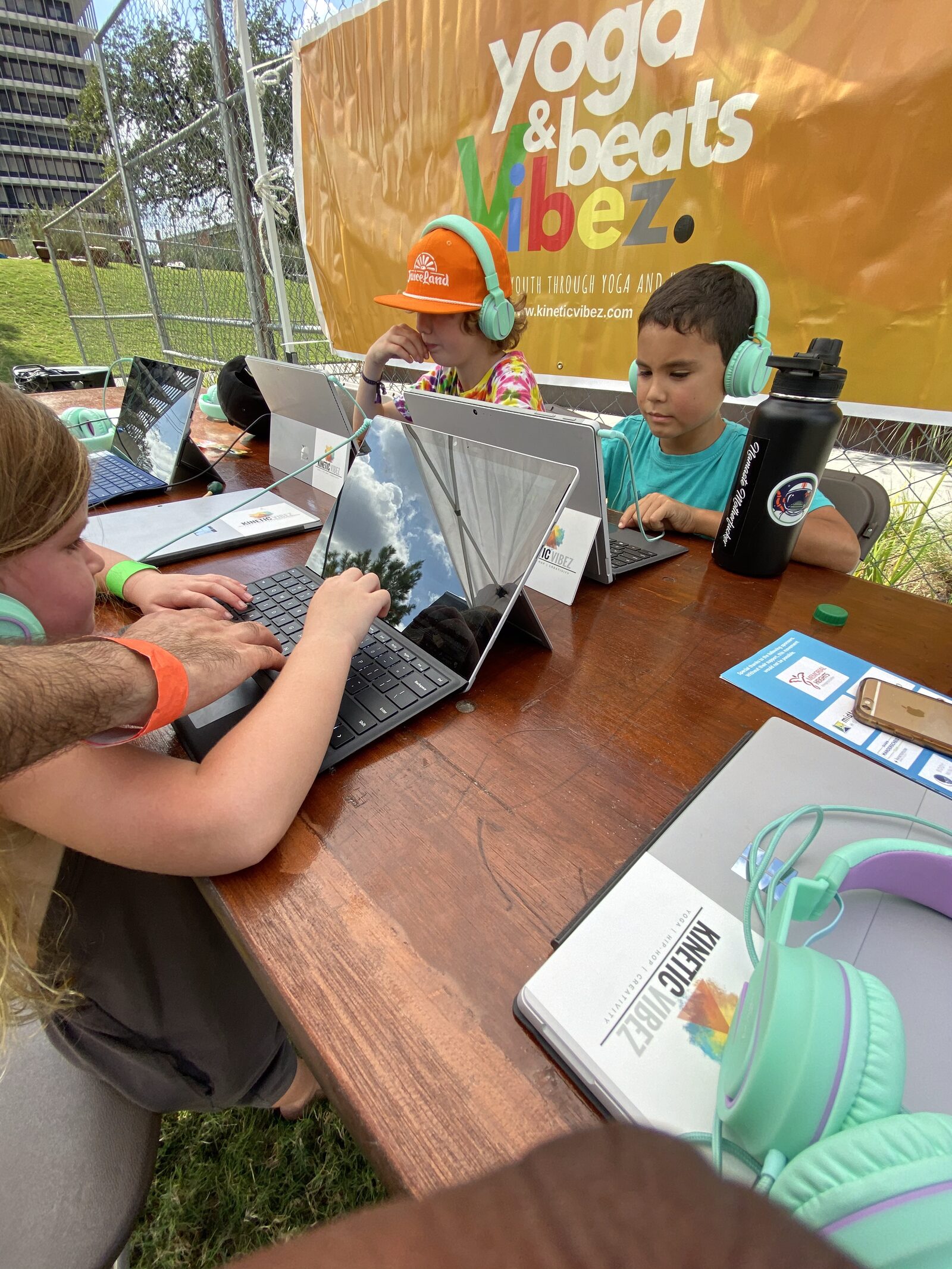 Students with teal headphones at outdoor Yoga & Beats Vibez event, Kinetic Vibez brochures and headphones on table in foreground