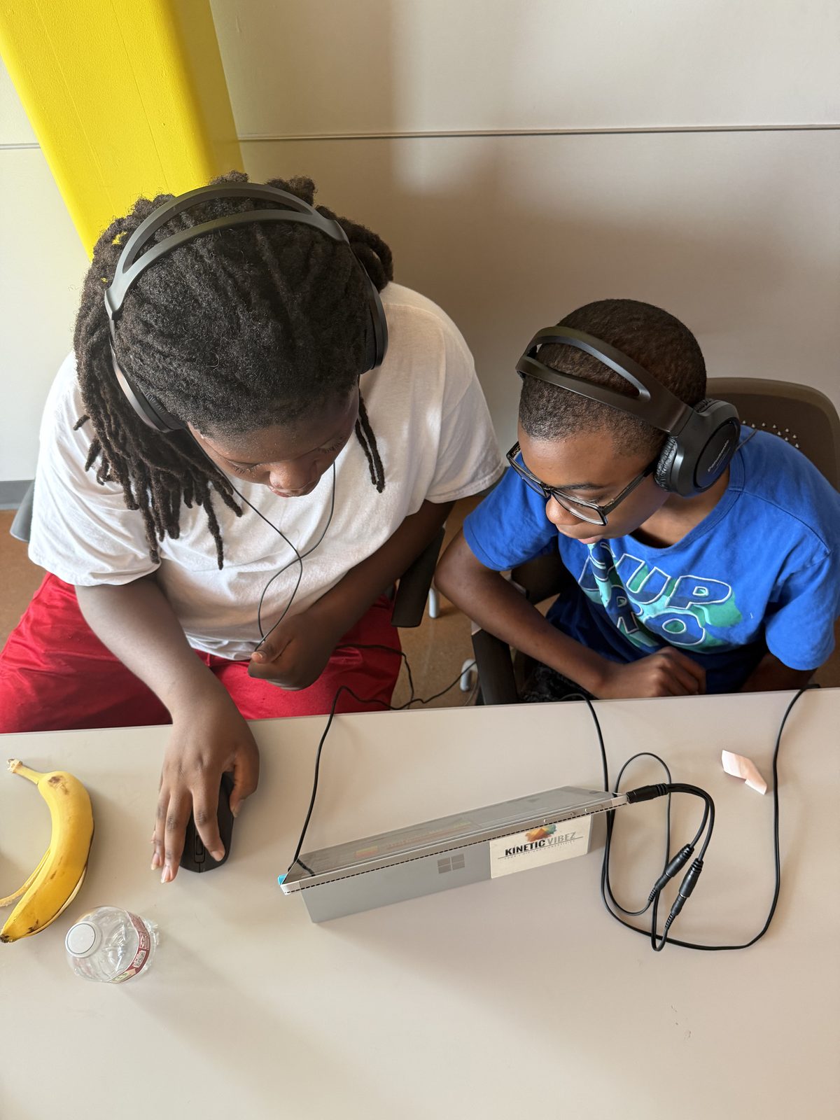 Two students with headphones working together on a Kinetic Vibez-branded Surface laptop during a music production session